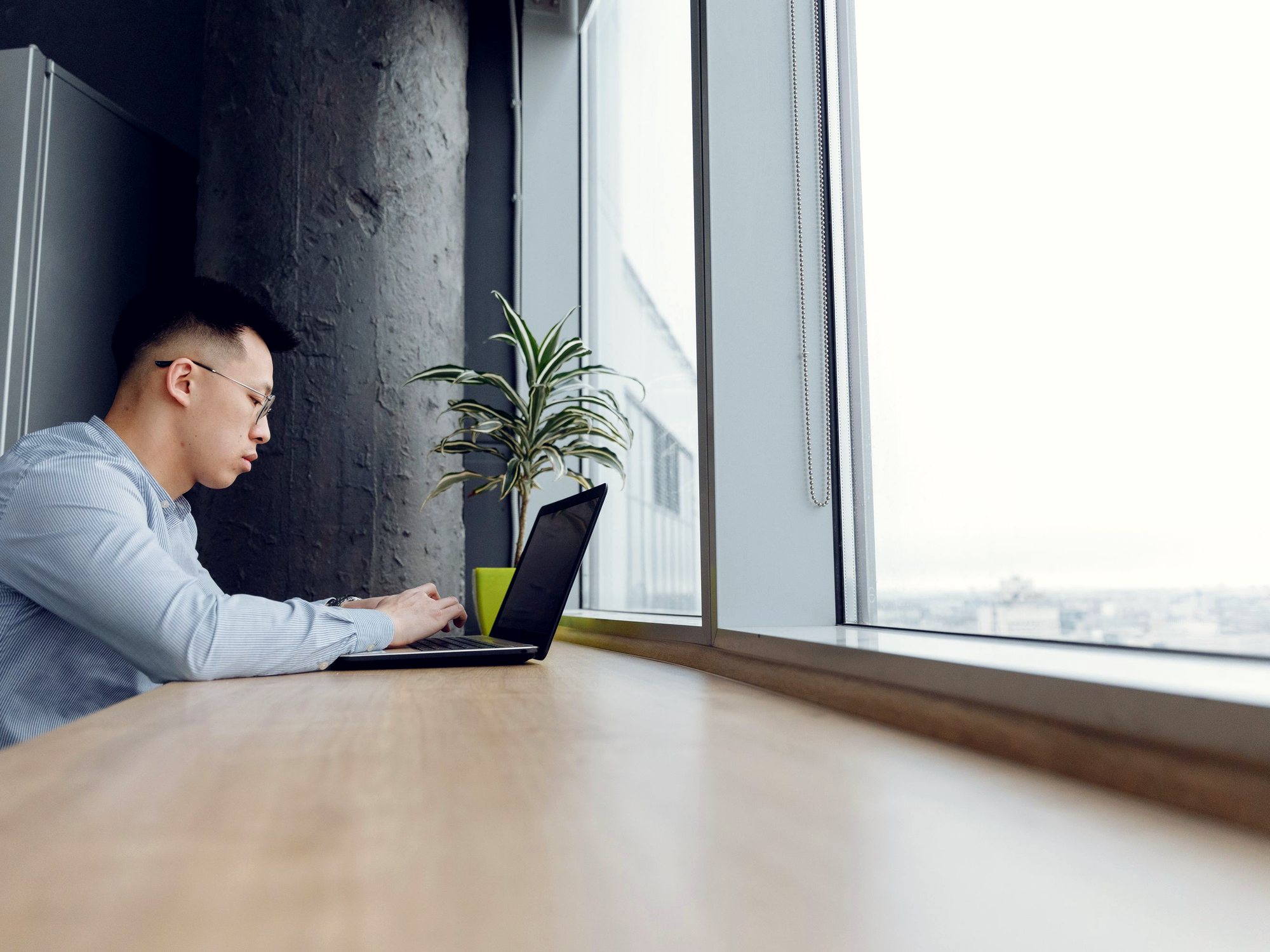 A woman working at a laptop beside a bright window